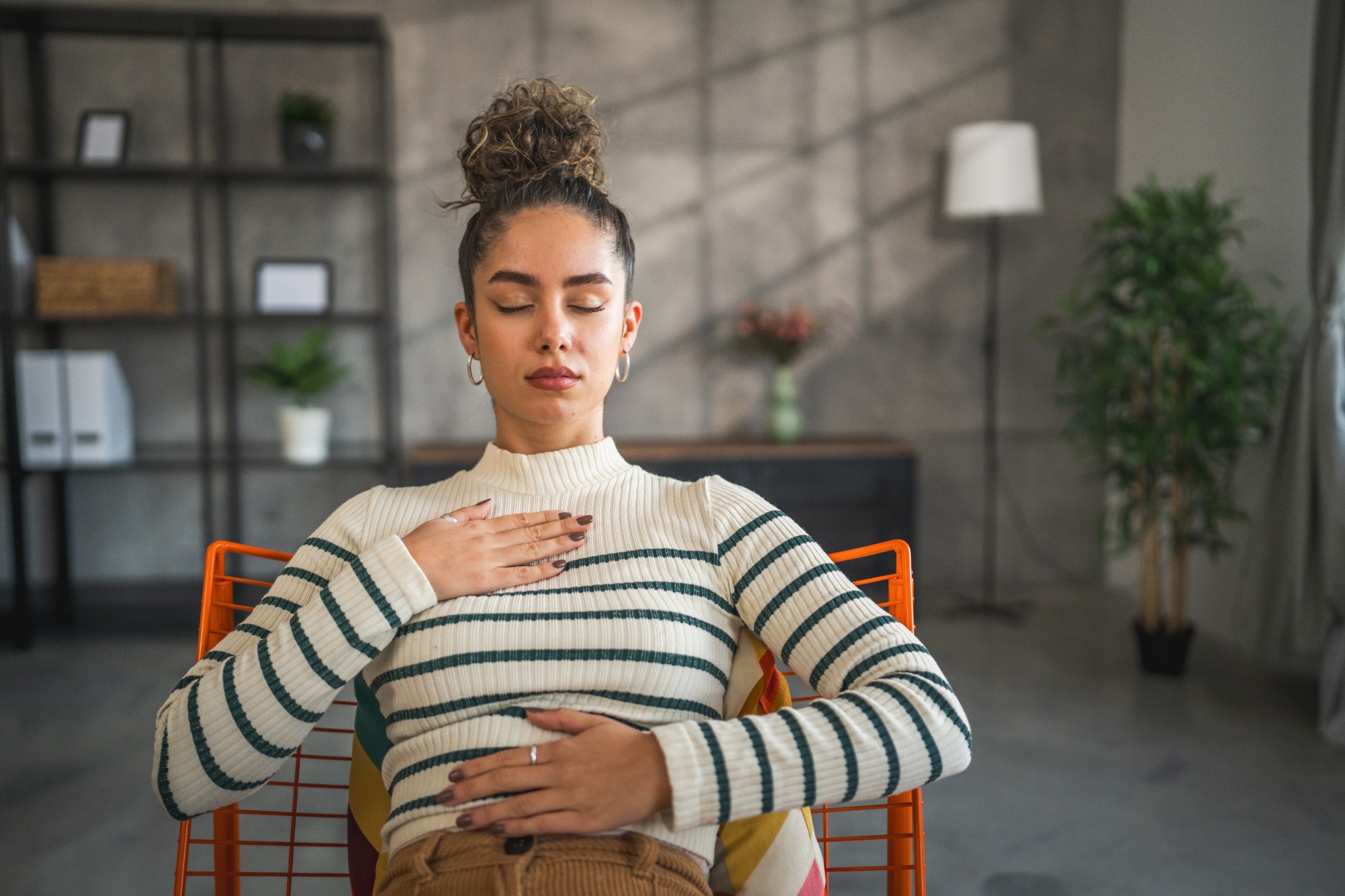 Woman practicing a grounding breath with one hand on her chest and one on her abdomen
